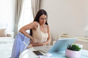 businesswoman-holding-her-back-while-working-laptop-home-office-desk-young-woman-stretching-sitting-feeling-her-back-tired-after-working-laptop-small-home-office-interior-774203