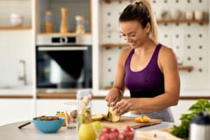 mulher-atletica-feliz-cortando-frutas-enquanto-prepara-uma-refeicao-saudavel-na-cozinha-496081