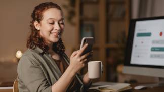mulher-em-casa-usando-smartphone-na-frente-computador-enquanto-toma-cafe